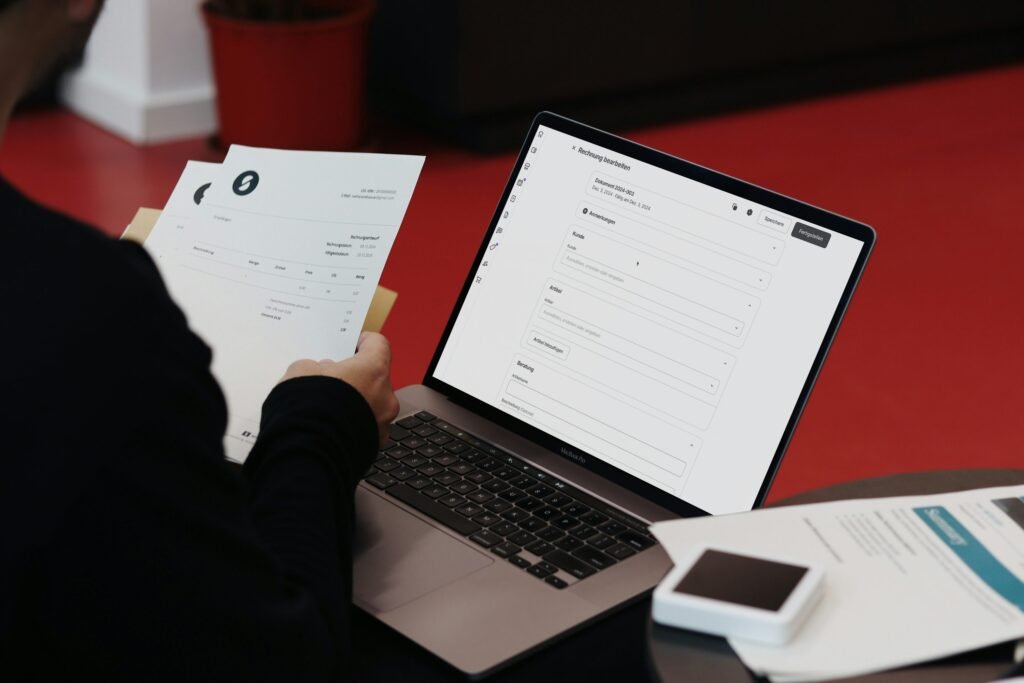 Business owner reviewing invoice documents beside a laptop